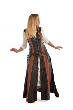 tam uzunlukta kahverengi deri fantezi kıyafeti, arkadaki kameraya pozuyla ayakta giymiş sarışın kız portresi. Beyaz stüdyo arka plan üzerinde izole.