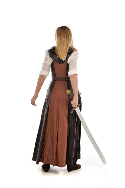 full length portrait of girl wearing brown  fantasy costume, holding a long sword, standing pose on white studio background. 