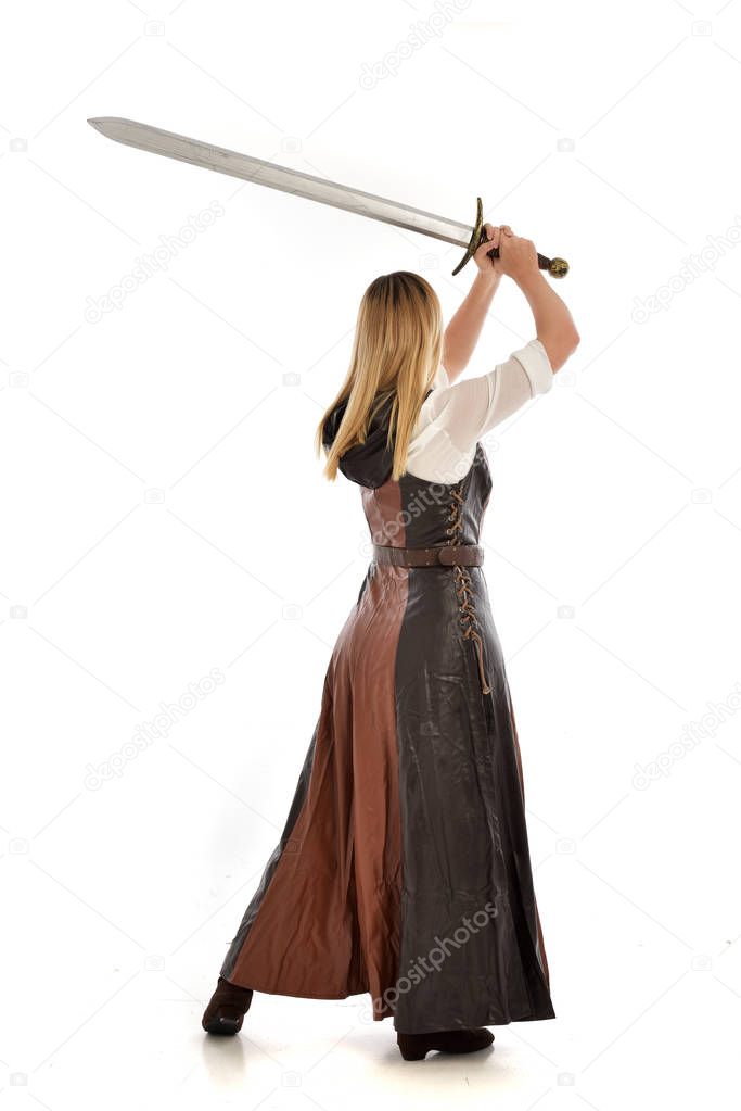 full length portrait of girl wearing brown  fantasy costume, holding a long sword, standing pose on white studio background. 