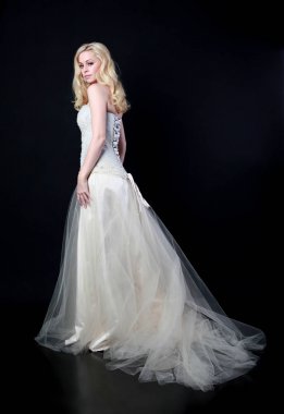 full length portrait of model wearing white bridal ball gown, standing pose on black background.