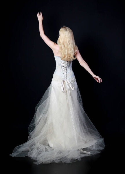 full length portrait of model wearing white bridal ball gown, standing pose on black background.