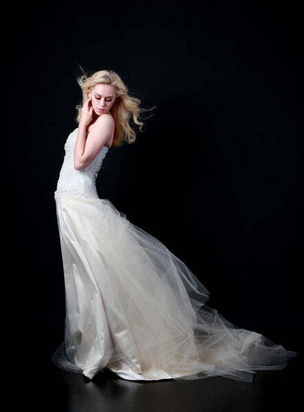 портрет модели в белом свадебном бальном платье, стоящей позы на черном фоне
.