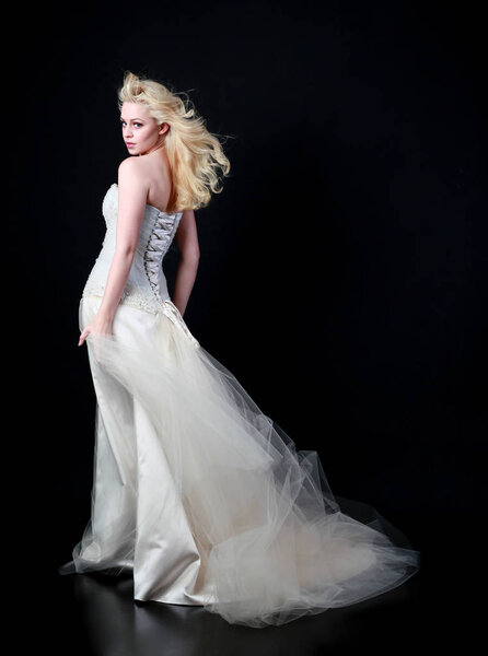 full length portrait of model wearing white bridal ball gown, standing pose on black background.