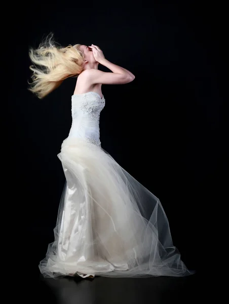 full length portrait of model wearing white bridal ball gown, standing pose on black background.