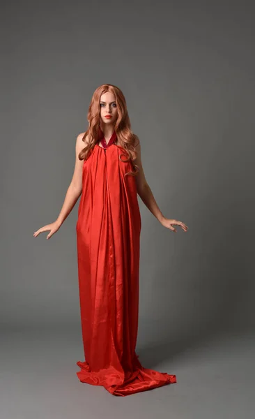 灰色スタジオ背景に立ちポーズの赤いシルクのドレスを着ている女性の完全な長さの肖像画 — ストック写真