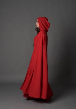 tam uzunlukta pelerin, ayakta poz gri studio arka plan üzerinde kırmızı fantezi Kostüm giymiş esmer Bayan portresi.