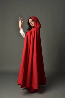 tam uzunlukta pelerin, ayakta poz gri studio arka plan üzerinde kırmızı fantezi Kostüm giymiş esmer Bayan portresi.