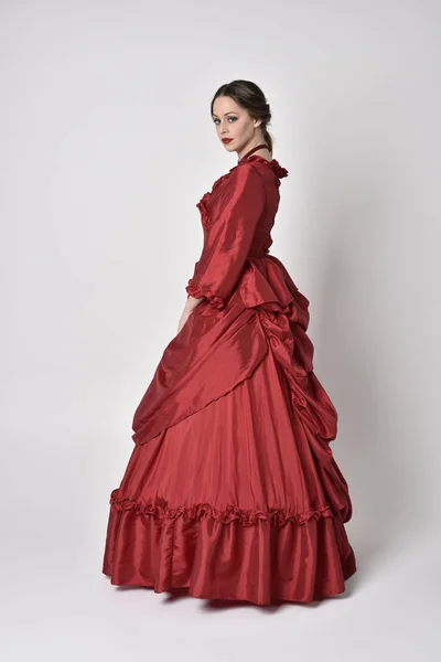 Pełnowymiarowy Portret Brunetki Czerwonej Jedwabnej Wiktoriańskiej Sukni Stojąc Tyłem Kamery — Zdjęcie stockowe