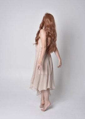 Çıplak, akıcı bir elbise ve kristal taç giyen güzel, peri bir kızın tam boy portresi. Gri bir stüdyonun arka planında ayakta ve dans pozu.