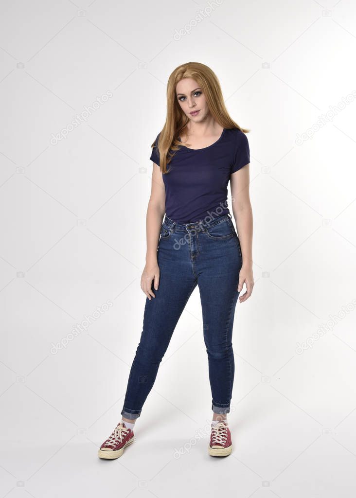Full length portrait of a pretty blonde girl wearing casual blue shirt, denim jeans and sneakers. Standing pose on a studio background.