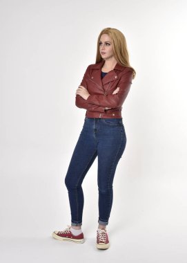 Kırmızı deri kot pantolon ve spor ayakkabı giyen sarışın güzel bir kızın tam boy portresi. Stüdyo arka planında poz vermek.