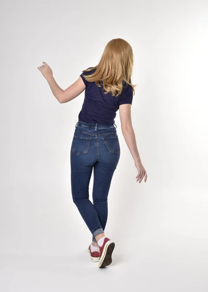 셔츠를 청바지와 운동화를 금발의 소녀의 자세를 취하고 카메라에서 스튜디오 위에서 — 스톡 사진