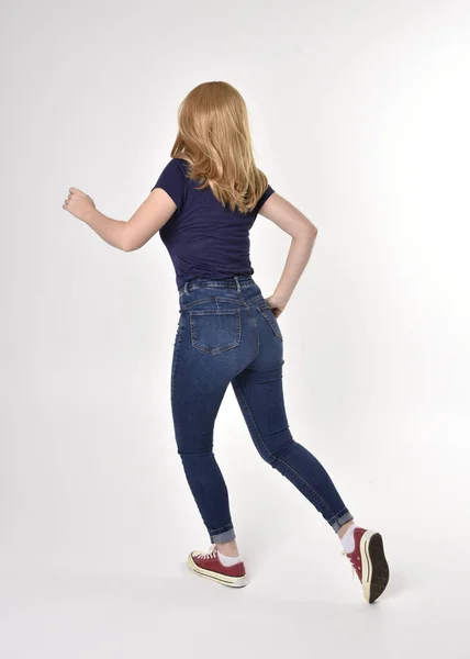 셔츠를 청바지와 운동화를 금발의 소녀의 자세를 취하고 카메라에서 스튜디오 위에서 — 스톡 사진