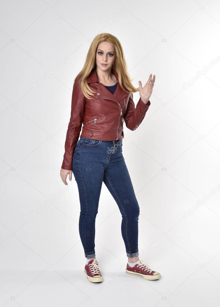 Full length portrait of a pretty blonde girl wearing red leather jacket denim jeans and sneakers. Standing pose  on a studio background.