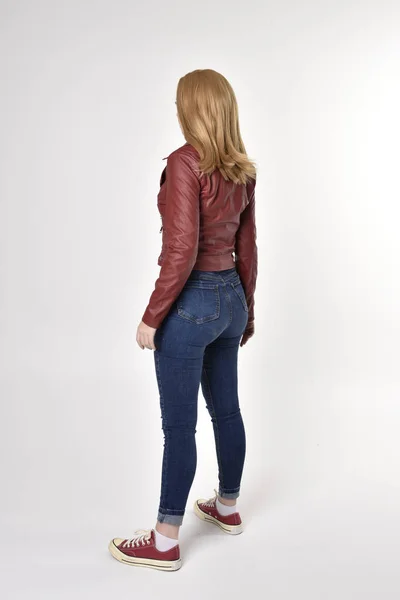 一个穿着红色皮夹克 牛仔和运动鞋的漂亮金发姑娘的全长肖像 站立姿势 面对着相机 在工作室的背景下 — 图库照片