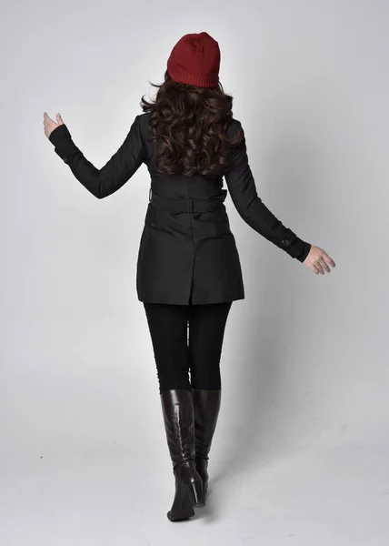 全长肖像一个漂亮的黑发女孩穿着黑色外套 皮靴和红色贝尼 站在灰色工作室背景上的姿势 — 图库照片