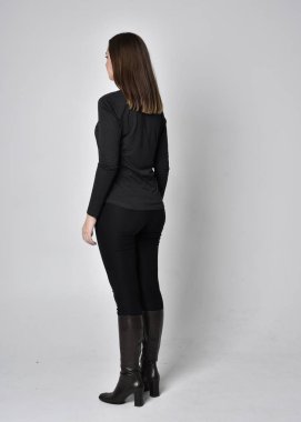 Siyah deri çizme giyen esmer güzel bir kızın tam boy portresi. Gri bir stüdyonun arka planında kameradan uzak durarak poz vermek..