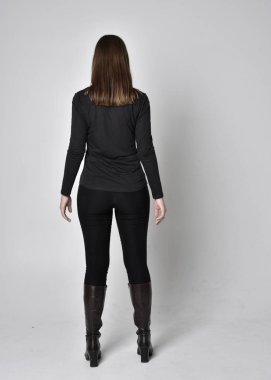 Siyah deri çizme giyen esmer güzel bir kızın tam boy portresi. Gri bir stüdyonun arka planında kameradan uzak durarak poz vermek..