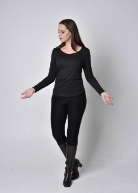 Siyah deri çizme giyen esmer güzel bir kızın tam boy portresi. Gri bir stüdyonun arka planında kameraya dönük duruyoruz..