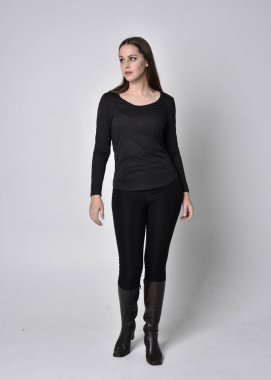 Siyah deri çizme giyen esmer güzel bir kızın tam boy portresi. Gri bir stüdyonun arka planında kameraya dönük duruyoruz..