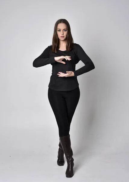 一个穿着黑色衬衫皮靴的漂亮的黑发女孩的全长肖像 站立姿势 面对着相机 在灰色的工作室背景上 — 图库照片