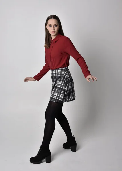 全长肖像一个漂亮的黑发女孩穿着红色衬衫和格子花裙与腿和靴子 在演播室背景上的站立姿势 — 图库照片