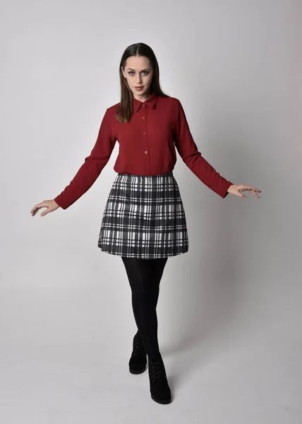 全长肖像一个漂亮的黑发女孩穿着红色衬衫和格子花裙与腿和靴子 在演播室背景上的站立姿势 — 图库照片