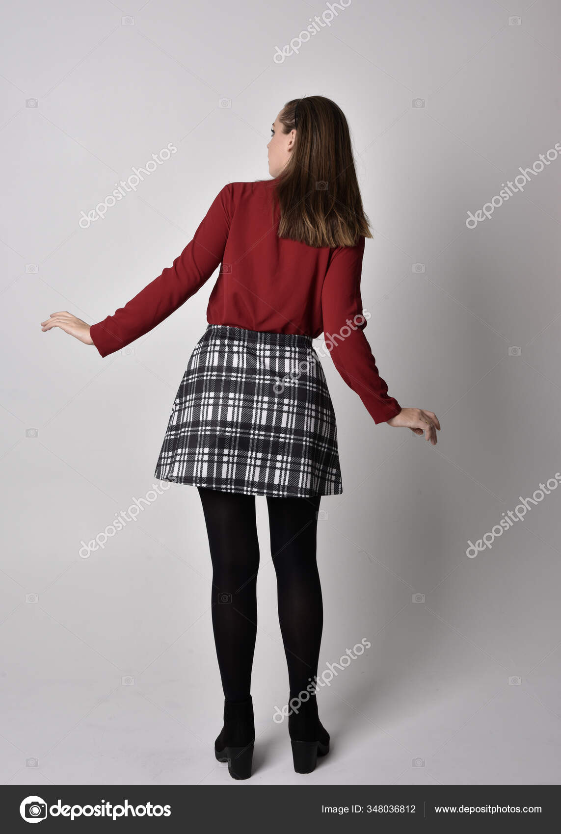 全长肖像一个漂亮的黑发女孩穿着红色衬衫和格子花裙与腿和靴子在摄影棚的背景下面对镜头站立的姿势