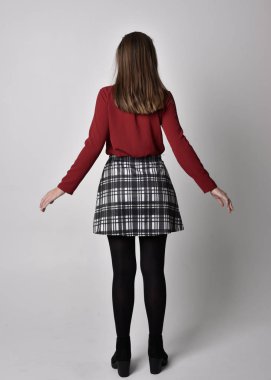 Uzun boylu, esmer, kırmızı tişörtlü, etekli, tozlu ve çizmeli güzel bir kızın portresi. Stüdyonun arka planında kameraya dönük poz vermek.