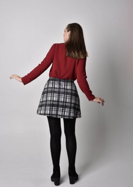 Uzun boylu, esmer, kırmızı tişörtlü, etekli, tozlu ve çizmeli güzel bir kızın portresi. Stüdyonun arka planında kameraya dönük poz vermek.