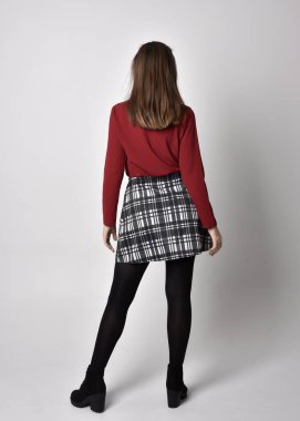 Uzun boylu, esmer, kırmızı tişörtlü, etekli, tozlu ve çizmeli güzel bir kızın portresi. Stüdyonun arka planında kameraya dönük poz vermek.