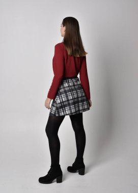 Uzun boylu, esmer, kırmızı tişörtlü, etekli, tozlu ve çizmeli güzel bir kızın portresi. Stüdyonun arka planında kameraya dönük poz vermek.