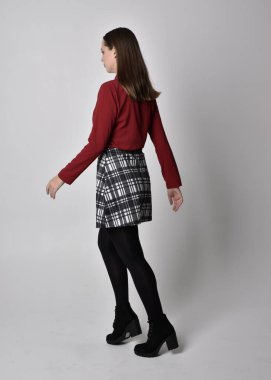 Uzun boylu, esmer, kırmızı tişörtlü, etekli, tozlu ve çizmeli güzel bir kızın portresi. Stüdyonun arka planında kameraya dönük poz vermek.