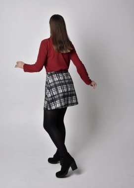 Uzun boylu, esmer, kırmızı tişörtlü, etekli, tozlu ve çizmeli güzel bir kızın portresi. Stüdyonun arka planında kameraya dönük poz vermek.