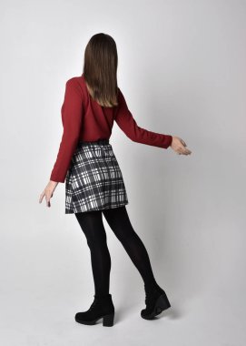 Uzun boylu, esmer, kırmızı tişörtlü, etekli, tozlu ve çizmeli güzel bir kızın portresi. Stüdyonun arka planında kameraya dönük poz vermek.