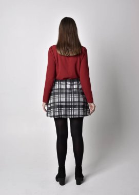 Uzun boylu, esmer, kırmızı tişörtlü, etekli, tozlu ve çizmeli güzel bir kızın portresi. Stüdyonun arka planında kameraya dönük poz vermek.