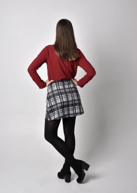 Uzun boylu, esmer, kırmızı tişörtlü, etekli, tozlu ve çizmeli güzel bir kızın portresi. Stüdyonun arka planında kameraya dönük poz vermek.