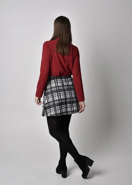 全长肖像一个漂亮的黑发女孩穿着红色衬衫和格子花裙与腿和靴子 在摄影棚的背景下 面对镜头站立的姿势 — 图库照片