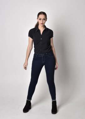 At kuyruklu, kot çizmeli ve siyah bluzlu güzel esmer bir kızın portresi. Stüdyo arka planında tam boy ayakta poz.