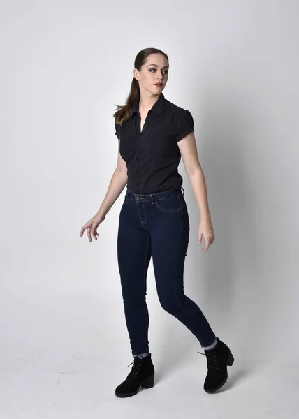 一个长着马尾辫 穿着牛仔裤靴和黑色衬衫的漂亮黑发女孩的画像 全长站立姿势在工作室的背景上 — 图库照片