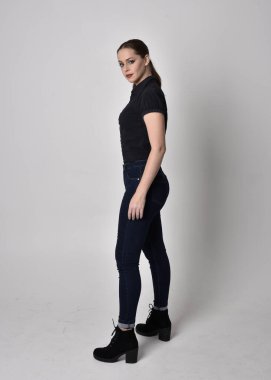 At kuyruklu, kot çizmeli ve siyah bluzlu güzel esmer bir kızın portresi. Stüdyonun arka planında, yan profilde tam boy poz.