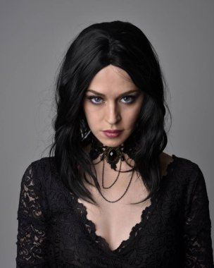 Stüdyo arka planında poz veren siyah saçlı güzel, gotik bir kızın yakın portresi..
