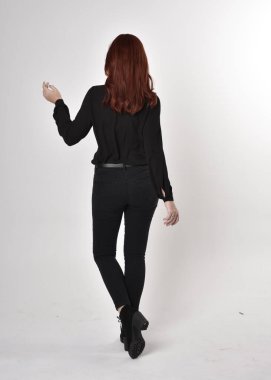 Siyah kot pantolon, bot ve bluz giyen kızıl saçlı güzel bir kızın portresi. Stüdyonun arka planında tam boy poz, kamera arkası....