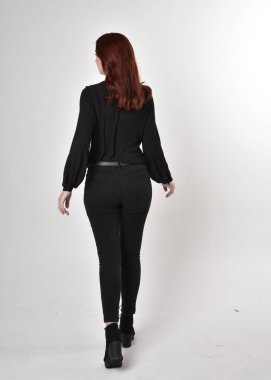 Siyah kot pantolon, bot ve bluz giyen kızıl saçlı güzel bir kızın portresi. Stüdyonun arka planında tam boy poz, kamera arkası....