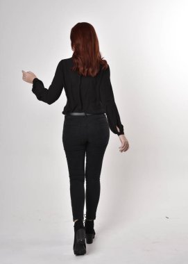 Siyah kot pantolon, bot ve bluz giyen kızıl saçlı güzel bir kızın portresi. Stüdyonun arka planında tam boy poz, kamera arkası....