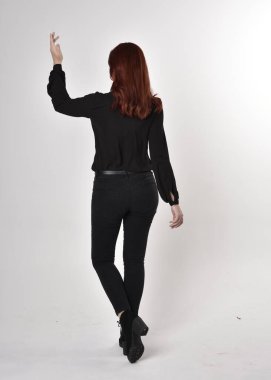 Siyah kot pantolon, bot ve bluz giyen kızıl saçlı güzel bir kızın portresi. Stüdyonun arka planında tam boy poz, kamera arkası....