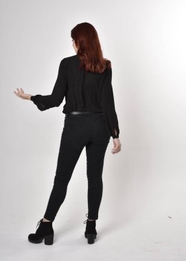 Siyah kot pantolon, bot ve bluz giyen kızıl saçlı güzel bir kızın portresi. Stüdyonun arka planında tam boy poz, kamera arkası....