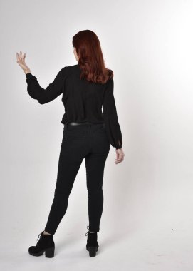 Siyah kot pantolon, bot ve bluz giyen kızıl saçlı güzel bir kızın portresi. Stüdyonun arka planında tam boy poz, kamera arkası....