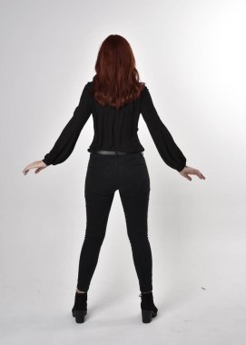 Siyah kot pantolon, bot ve bluz giyen kızıl saçlı güzel bir kızın portresi. Stüdyonun arka planında tam boy poz, kamera arkası....
