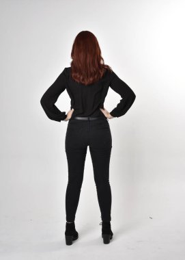 Siyah kot pantolon, bot ve bluz giyen kızıl saçlı güzel bir kızın portresi. Stüdyonun arka planında tam boy poz, kamera arkası....